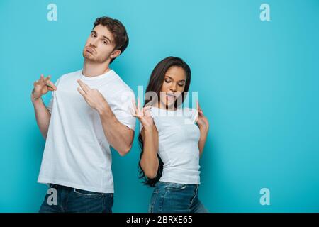 sceptical man and flirty african american girl touching white t-shirt on blue background Stock Photo