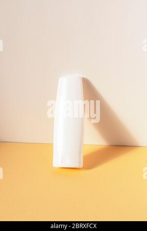 Cosmetic white unbranded plastic bottle on yellow table. Natural skincare products concept. Stock Photo