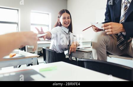 Classmates having fun during free period in classroom. Boys and girls passing some notes and smiling in classroom. Stock Photo