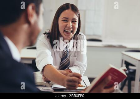 Two students talking and smiling in classroom. Young girl talking with her classmate in high school classroom. Stock Photo