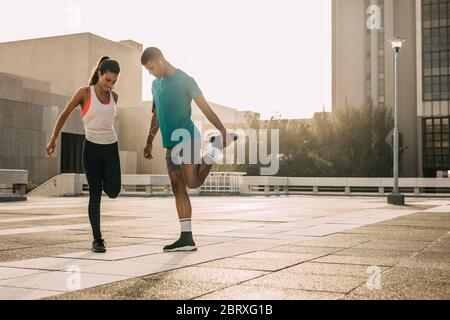 Fitness man and woman stretching together outdoors. Two people working out in morning in the city. Stock Photo