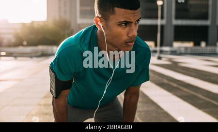Sportsman standing bent over and resting after a running session in city. Fitness man taking break after a run. Stock Photo