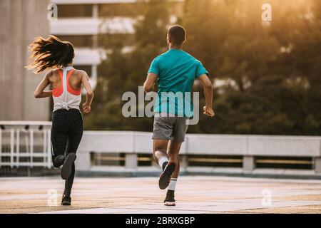 Rear view of a man and woman running together in morning. Friends in sportswear jogging together in the city. Stock Photo