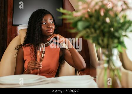 selective focus of dreamy african american woman holding glass of champagne in private jet Stock Photo