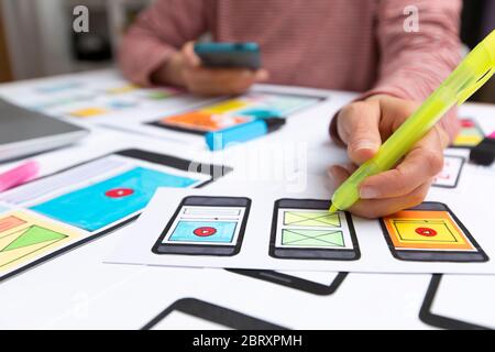 The web designer is working on an interface to mobile phone applications. The developer draws sketches of user applications for smartphones. Stock Photo