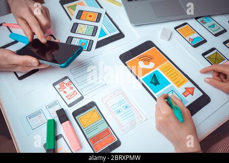 The web designer is working on an interface to mobile phone applications. The developer draws sketches of user applications for smartphones. Stock Photo