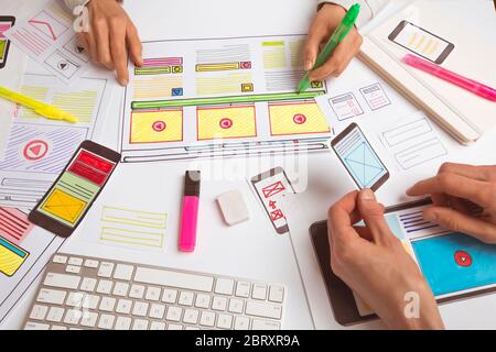 A website designer is working on an application interface. The developer draws sketches of user applications for smartphones. Stock Photo