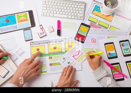 A website designer is working on an application interface. The developer draws sketches of user applications for smartphones. Stock Photo