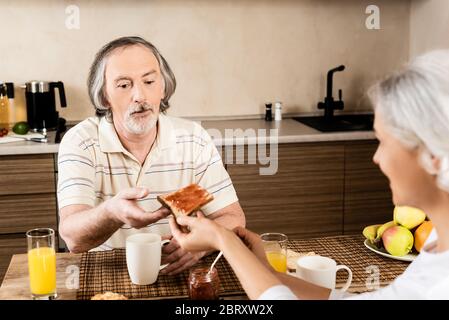 selective focus of mature woman giving sweet toast bread with jam to husband Stock Photo
