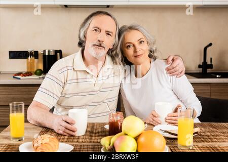 happy mature couple looking at camera near breakfast on table Stock Photo