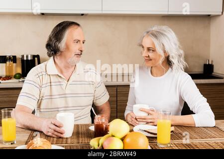 happy mature couple looking at each other near breakfast on table Stock Photo