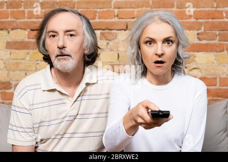 selective focus of surprised and mature couple watching movie in living room Stock Photo