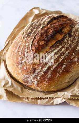 Fresh loaf of sourdough bread on a crumpled brown paper bag Stock Photo