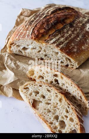 Fresh sourdough loaf and slices from the bakery on a crumpled brown paper bag Stock Photo