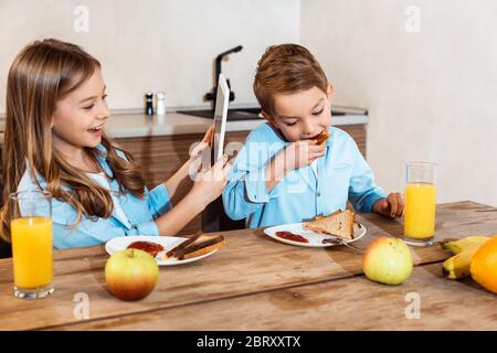 happy kid using digital tablet near brother eating toast bread with jam Stock Photo