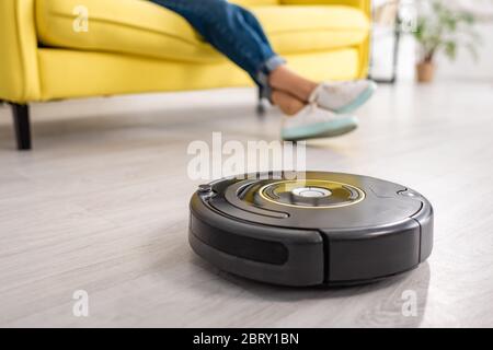 Cropped view of female legs with robotic vacuum cleaner on floor in living room Stock Photo