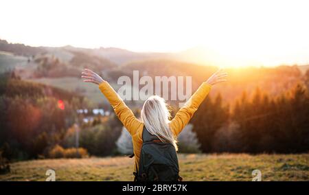 Rear view of senior woman hiker standing outdoors in nature at sunset. Stock Photo
