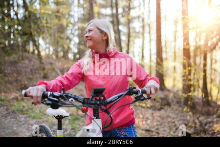 Active senior woman with e-bike cycling outdoors in nature. Stock Photo