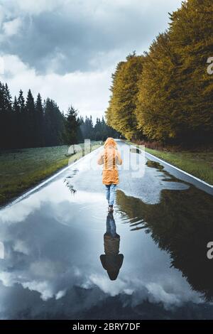 Walking alone concept. Rear view of a woman hiker wearing a yellow jacket walking alone on mountain highway in summer foggy day in Transylvania, Roman Stock Photo