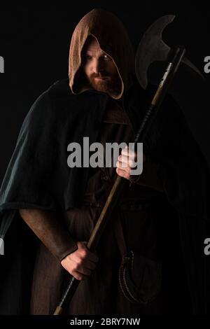 frowning medieval Scottish warrior with battle axe in mantel isolated on black Stock Photo
