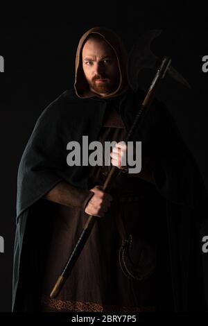 frowning medieval Scottish warrior with battle axe in mantel isolated on black Stock Photo