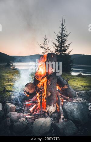 Small campfire with gentle flames beside a lake during a glowing sunset. Belis, Cluj, Romania Stock Photo