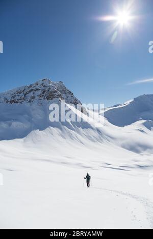 one women snowshoeing towards Valbellhorn mountain in winter landscape, sun, blue sky Stock Photo