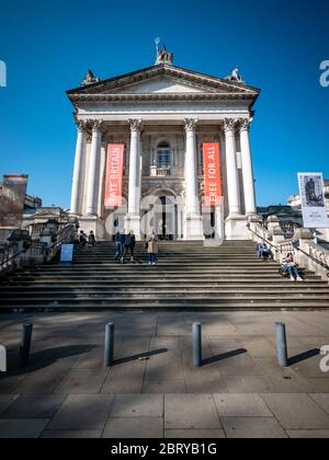 The Tate Britain museum and gallery on Millbank, Westminster, with visitors milling around the entrance and sitting on the stairs.