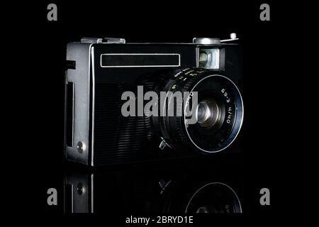 One whole dark vintage camera isolated on black glass Stock Photo