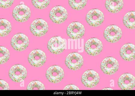 Pattern made of ring donuts with white glaze and clourful hundreds and thousands on pink background Stock Photo