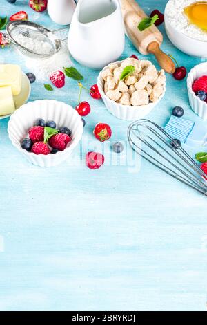 Berry cake baking recipe. Summer cooking baking background with assorted berries, baking ingredients, tools and utensils, light blue sun lighted woode Stock Photo