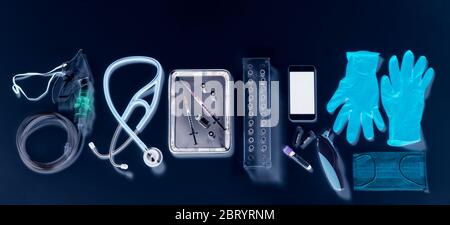 Potential way out of lockdown stage. Medical equipment on a black background, oxygen mask, stethoscope, mobile phone with a contact tracing app, syringes for vaccine, blue gloves and digital thermometer. Stock Photo