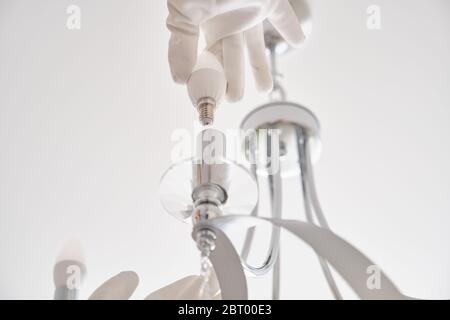 Woman installs LED lights in new ceiling chandelier Stock Photo