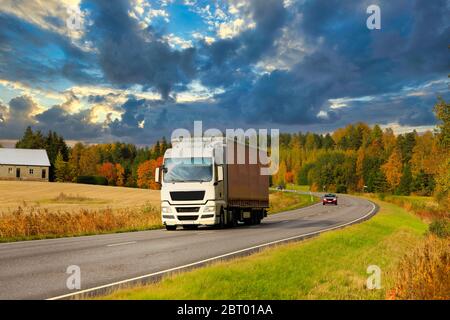 White semi trailer truck on highway at speed transporting goods on a beautiful autumn evening. Stock Photo