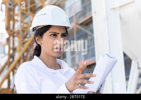 Female architect wearing white hard hat working on construction site. Stock Photo