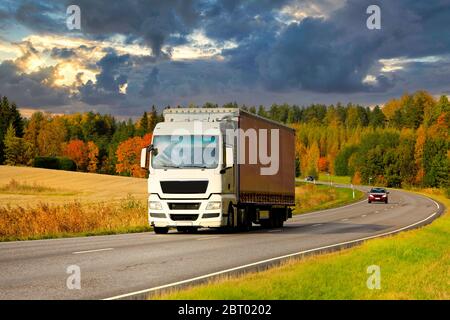 White semi trailer truck on highway at speed transporting goods on a beautiful autumn evening. Stock Photo