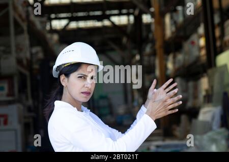Female architect wearing white hard hat working on construction site, looking at camera. Stock Photo