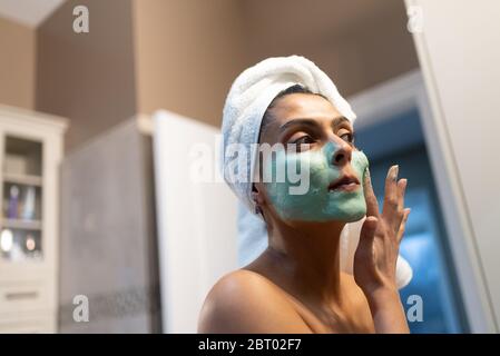 Woman standing in bathroom, applying face mask after bath. Stock Photo