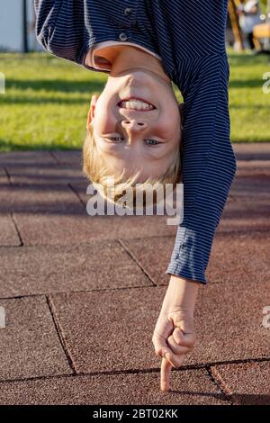 Boy upside down leaning on a finger outoors in the park. Concept for young people who do things easily Stock Photo