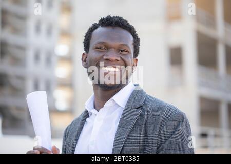 Portrait of smiling young man with short hair wearing white shirt and grey jacket, looking at camera. Stock Photo