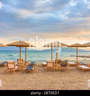 Picturesque view of beach with rows of straw umbrellas by the sea at sunset Stock Photo