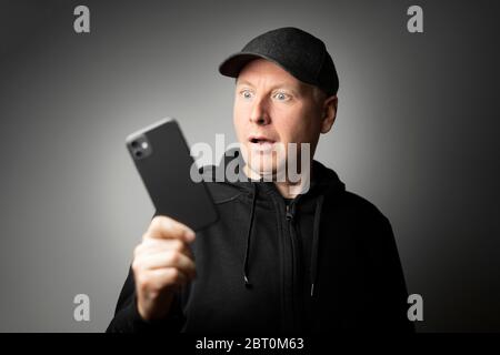 Man in black clothes shocked with the message on the phone or phone itself Stock Photo