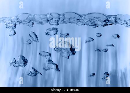 Image composition of format-filling view of rising air bubbles under a row of connected air bubbles on the water surface against a structured blue bac Stock Photo