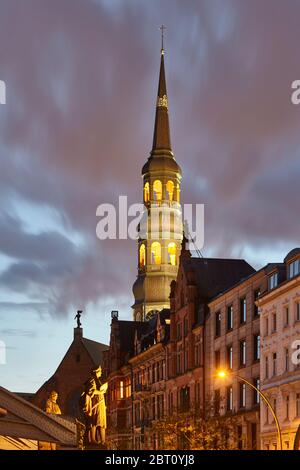 The illuminated steeple of St Katharinen close to the Speicherstadt in Hamburg. In front the statues of Christoph Columbus and Vasco da Gama at the Ko Stock Photo