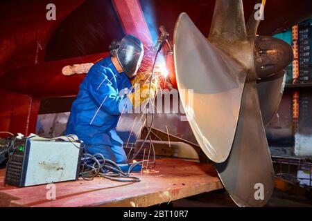 A worker electro-welds ship's screw of the tanker ship Koesterberg of the Vega-Shipping Company in the floating dock of the Norderwerft Repair in the Stock Photo