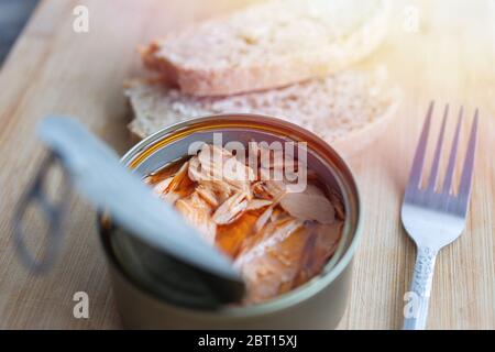 Close up of open canned tuna in red oil, fork and bread on wooden table, top view Stock Photo