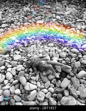 Multi coloured rainbow next to a woman lying on rocks Stock Photo