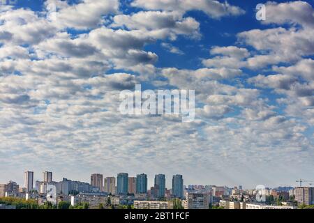 The sun's rays brightly illuminate the white-gray clouds in the blue sky above the awakening city. Shining light in the cloudy morning sky. Stock Photo
