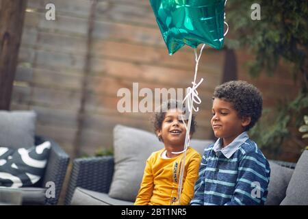 Little afro-american brother and sister sitting together outdoor and play with balloon. Stock Photo