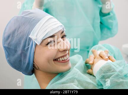 Happy female patient smiling and showing thumb up gesture with professional dentists during appointment in modern office in clinic Stock Photo